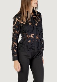 Zwarte kanten blouse met bloemen uitsparingen, lange mouwen en een knoopsluiting aan de voorkant, gecombineerd met strakke zwarte broeken.