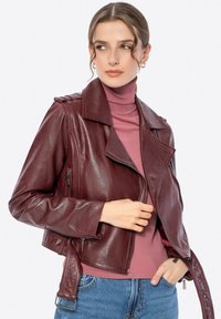 Bordeaux leren bikerjack met een cropped ontwerp, ingesneden kraag, ritszakken en zilveren hardwareaccenten. Draagt over een lichtroze coltrui.