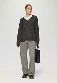 Schwarzer gestrickter Pullover mit glitzernden Fäden, V-Ausschnitt, kombiniert mit hellgrauen Hosen und einer schwarzen Tasche. Strukturierter Stoff und lockere Passform.