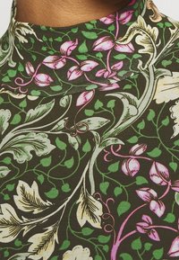 Höghalströja med blommönster på mörkgrön botten, med rosa och vita blommor, gröna blad och en mjuk, stretchig textur.