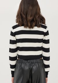 Maglione corto a righe bianco e nero con texture a coste e maniche lunghe. Abbinato a pantaloni in pelle nera a vita alta.