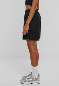 Pantaloni scurți negri pentru sport, cu talie elastică, fante laterale și o croială lejeră, asortați cu adidași gri și șosete albe până la gleznă.