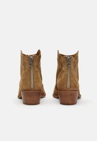 Bottines en suède marron avec une finition texturée et de petites perforations, dotées d'une fermeture éclair en métal argenté à l'arrière et d'un petit talon en bois.