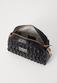 Borsa a mano in pelle nera con texture trapuntata, hardware dorato e chiusura zip. L'interno presenta una fodera chiara e un comparto etichettato visibile.
