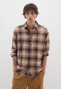 Camicia a quadri marrone e crema con vestibilità rilassata, caratterizzata da maniche arrotolate e una tasca sul petto.