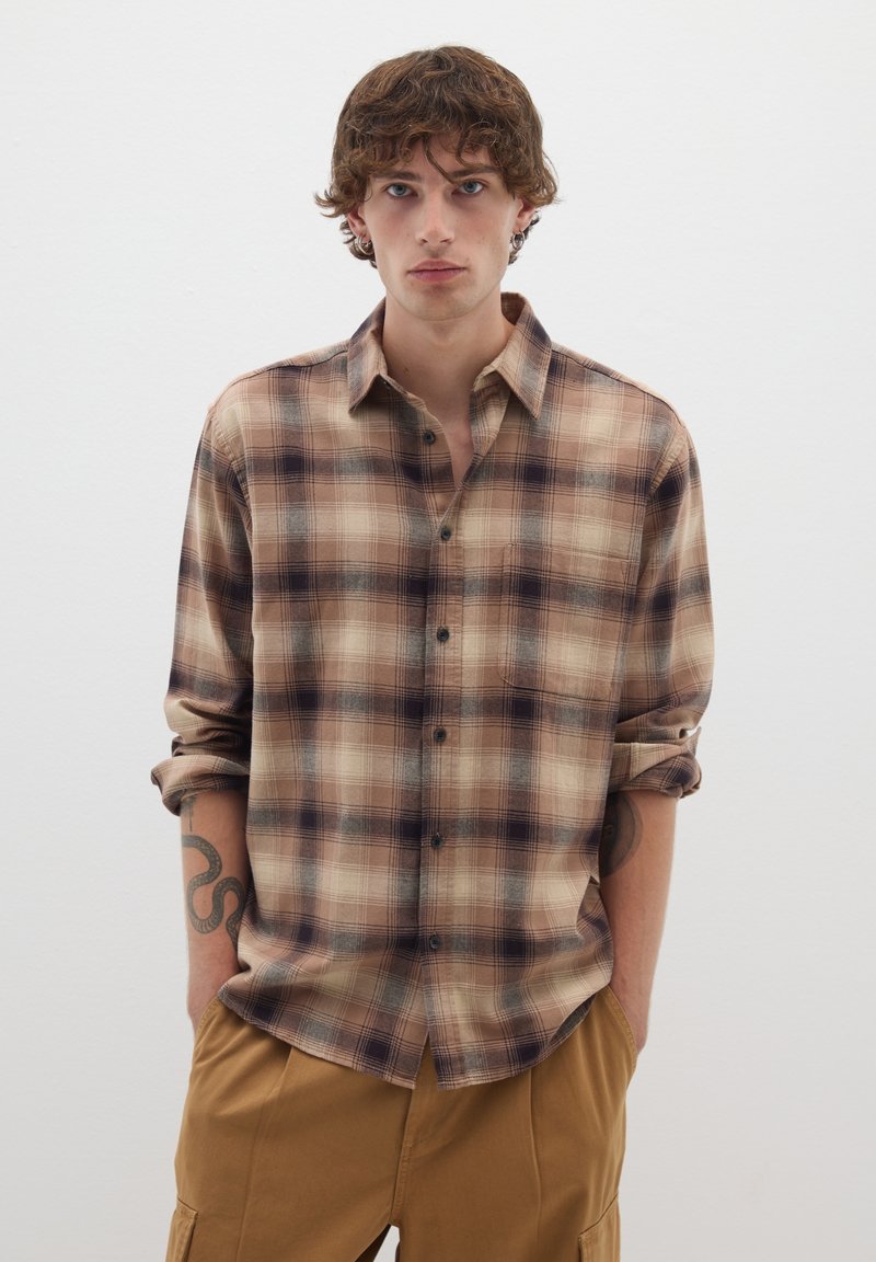 Camicia a quadri marrone e crema con vestibilità rilassata, caratterizzata da maniche arrotolate e una tasca sul petto.