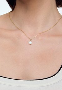 Naszyjnik z łańcuszkiem w odcieniu złota z okrągłym wisiorkiem z opalu. Łańcuszek ma delikatny, teksturowany wzór i subtelną poświatę.