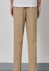 Pantalon kaki à coupe droite, tissu en coton lisse, pli central, style épuré et minimaliste.