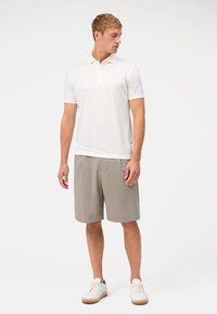 Witte polo met korte mouwen, drie knoopsluiting, gecombineerd met lichtgrijze shorts en witte sneakers. Glad materiaal, geen zichtbare patronen.