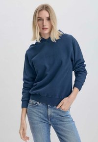 Felpa blu navy in tessuto morbido, con cappuccio regolabile, polsini e orlo a coste, abbinata a jeans chiari.