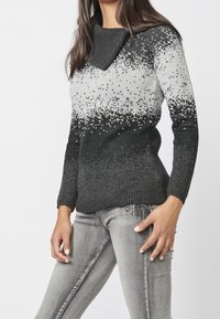 Pull tricoté dégradé noir et gris avec un col côtelé et des manches longues, présentant une finition texturée et des embellissements subtils le long de l'ourlet.