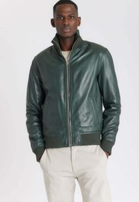 Groene leren bomberjack met een hoge kraag, voorsluiting met rits en ribbelmanchetten. Gladde textuur en twee zijzakken.
