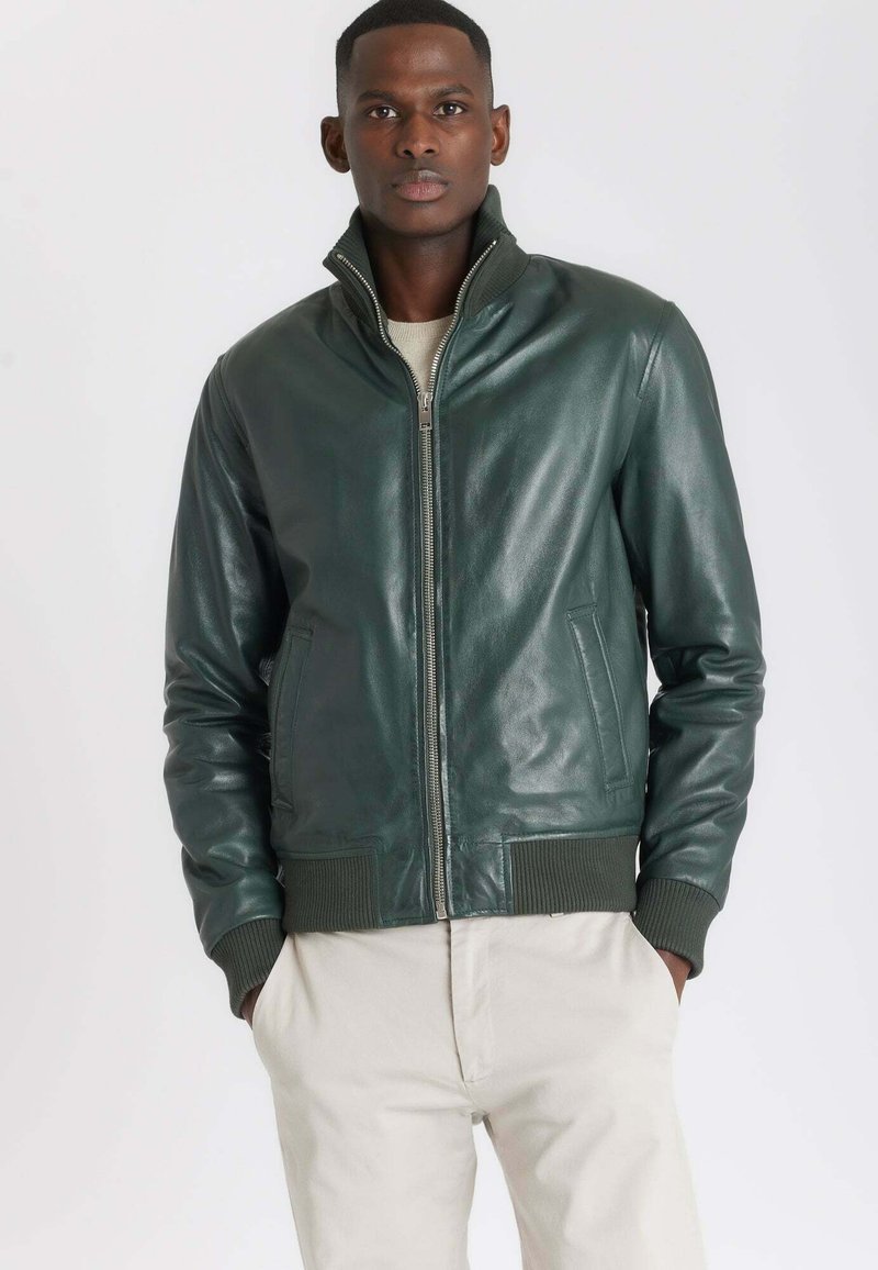 Groene leren bomberjack met een hoge kraag, voorsluiting met rits en ribbelmanchetten. Gladde textuur en twee zijzakken.