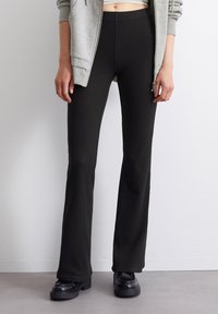 Mustat ribbed-hyppypöksyt, joissa on joustava vyötärö, teksturoidun pinnan ja tiukan istuvuuden omaavat reidet, yhdistettynä alustasaappaisiin.