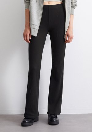 Mustat ribbed-hyppypöksyt, joissa on joustava vyötärö, teksturoidun pinnan ja tiukan istuvuuden omaavat reidet, yhdistettynä alustasaappaisiin.