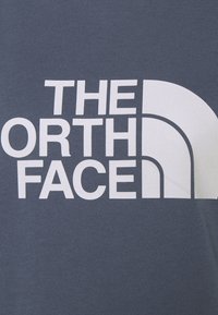 Niebieska bawełniana koszulka z dużym białym napisem "THE NORTH FACE" oraz logo w kształcie półksiężyca. Gładka tekstura, fason z okrągłym dekoltem.