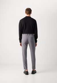 Men's outfit featuring a black long-sleeve top, gray tailored trousers, and black shoes. The trousers have subtle back pockets and a slim fit.
