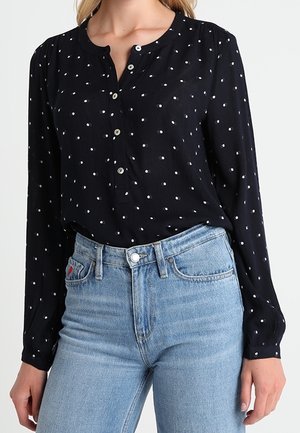 Dunkelblaues Langarmhemd mit weißen Punkten, Knopfverschluss am Hals, leichter Stoff, kombiniert mit hoch taillierten hellblauen Jeans.