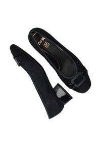 Ballerines en suède noir avec un talon bloc en vernis, présentant un détail de boucle décoratif sur le bout. Semelle intérieure douce pour le confort.