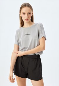 Lys grå, kortærmet træningsshirt med meshstruktur, med teksten "GOOD ENERGY". Sammen med sorte, løstsiddende shorts med elastisk talje.