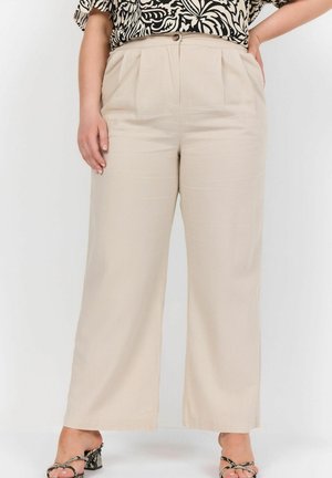 Pantalons larges beiges avec des plis à l'avant, une fermeture à bouton et une texture lisse. Associés à un haut noir et blanc à motifs.