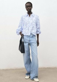 Blouse en voile léger à motif floral bleu clair, coupe décontractée, avec des manches bouffantes. Associée à un jean en denim moyen à jambes larges et un sac à main noir.