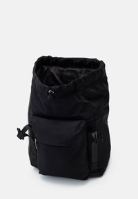 Mochila negra con parte superior ajustable, un bolsillo frontal con cremallera y correas laterales ajustables. Fabricada con un material duradero de textura suave.