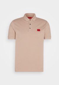 Polo beige à manches courtes avec col, trois boutons foncés et une petite étiquette rouge portant l'inscription "HUGO" sur la poitrine gauche.