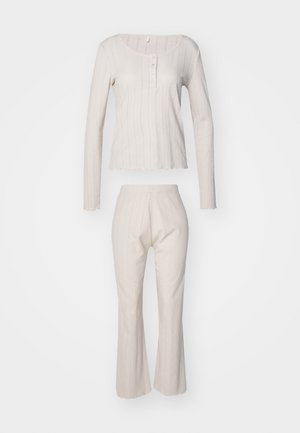 Ljust beige lounge-set, bestående av en långärmad topp med ribbstickad textur och knappdetalj, paired med ribbstickade, utsvängda byxor.