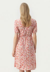Kukallinen mekko vaaleanpunaisena, punaisilla ja oransseilla kukilla, lyhyillä puffihihoilla, istuvalla vyötäröllä ja röyhelöhelmalla. Pehmeä kangastuntu.