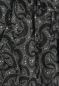 Tissu noir à surface texturée présentant un motif tourbillonnant de points blancs et d'étoiles. Des accents froncés ajoutent de la dimension au design.