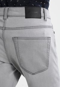 Jeans in denim grigio con una texture liscia, patch in pelle nera a contrasto sulla vita e design standard delle tasche posteriori.