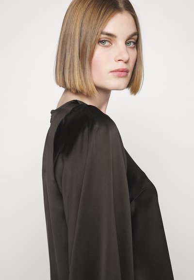 Blouse en satin noir avec des manches longues et fluides. Le design présente un subtil éclat et un col rond, créant une silhouette épurée.