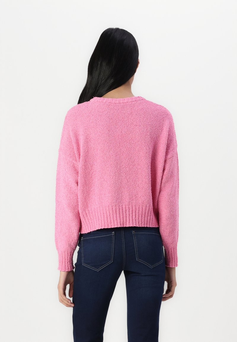 Rosa, verkürzter Pullover aus weichem, strukturiertem Material mit langen Ärmeln und geripptem Saum, kombiniert mit dunkelblauen Jeans.