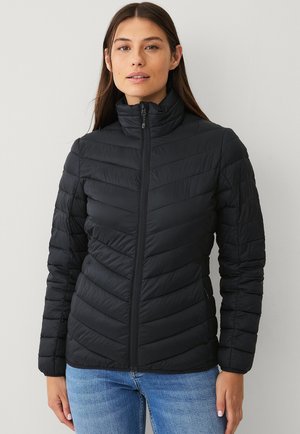 Zwarte pufferjack met een staande kraag, horizontale en chevron quilting, volledige rits aan de voorkant en lange mouwen, gecombineerd met blauwe jeans.