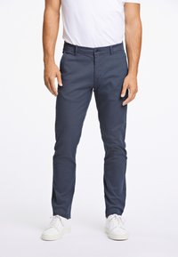 Chino blu navy in cotone morbido, con chiusura a bottone e passanti per cintura, abbinati a sneakers bianche a basso profilo.