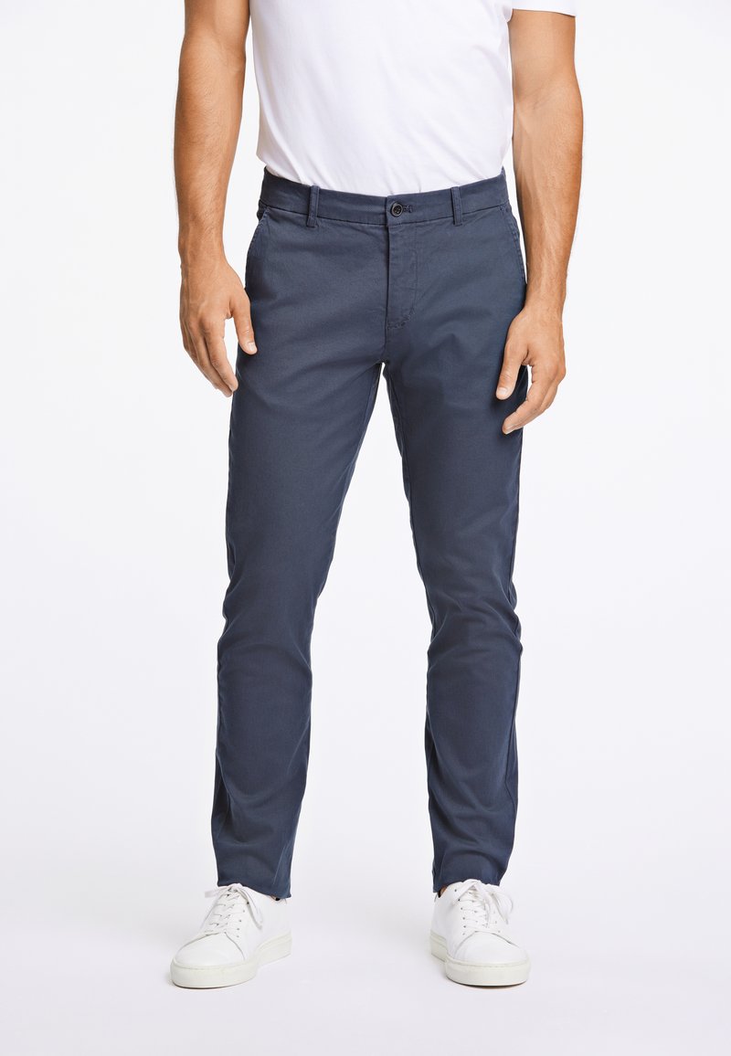 Chino blu navy in cotone morbido, con chiusura a bottone e passanti per cintura, abbinati a sneakers bianche a basso profilo.