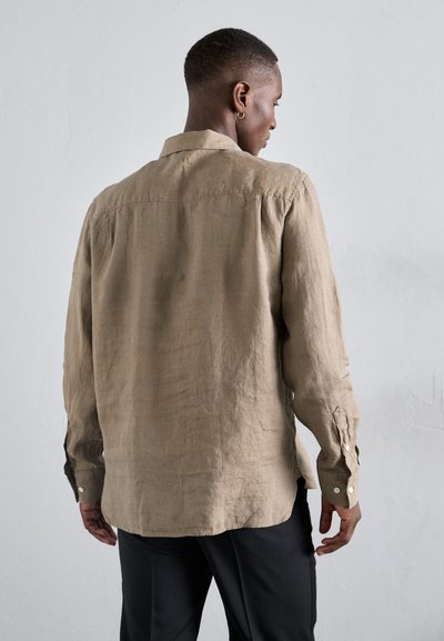 Beige linneskjorta med lång ärm, knappad manschett och ryggveck, parat med svarta byxor; den texturerade tyget ger ett avslappnat utseende.
