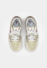 Beige and white leather sneakers with red accents and perforated toe. Flat white laces. Features Air Jordan logo on tongue and sides.