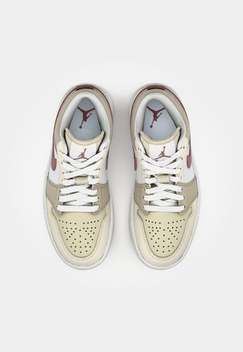 Baskets en cuir beige et blanc avec des accents rouges et un bout perforé. Lacets blancs plats. Présente le logo Air Jordan sur la languette et sur les côtés.