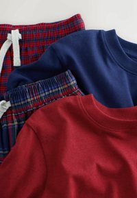 Tre beklædningsgenstande: en rød bomulds sweatshirt, en marineblå bomulds sweatshirt, og flannel loungebukser med et ternet mønster i rød, blå og gul.