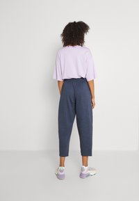 Lös passande ljuslila t-shirt och mörkblå avsmalnande sweatpants, matchat med flerfärgade sportskor. Slätt tyg, avslappnad design.