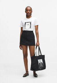 Valge T-särk, millel on kassigraafika, koos musta mini-seeliku ja musta kottiga, millel on inimese graafika. Mustad lamedad kingad.