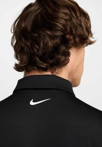 Czarna koszulka polo z kołnierzykiem, z białym logo Nike na plecach. Materiał wydaje się gładki z delikatnym połyskiem.