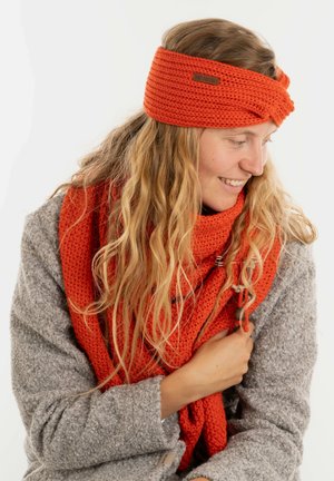 Gehaakte oranje sjaal verweven met een oranje haarband. De sjaal heeft een gestructureerd, chunky patroon; de haarband heeft een gedraaid ontwerp.