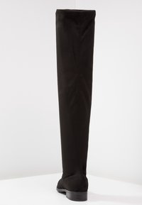 Bota negra por encima de la rodilla hecha de ante suave con un asta ajustada, punta redondeada y tacón bajo de bloque, que presenta un diseño sin costuras.