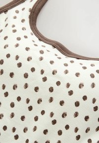 Tissu côtelé blanc avec des pois marron irréguliers et un col côtelé marron, suggérant un gros plan d'un haut ou d'une robe.