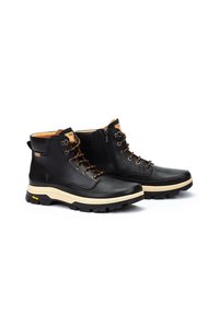 Botas de cuero negro con un collar acolchado, cordones marrones, cremallera lateral y suela de color crema. Suela de goma texturizada para mayor tracción.