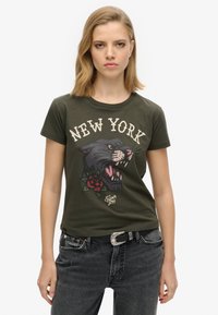 T-shirt en coton olive vert avec un graphique d'un panthère noire rugissant et des roses rouges, avec le texte "NEW YORK" en crème. Manches courtes, col rond.