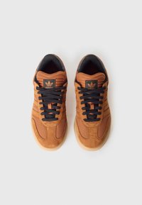 Ténis em camurça castanha e malha com atacadores pretos, língueta almofadada preta e solas de borracha com acabamento texturizado. Design clássico de três riscas.